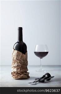 Paper bag with bottle of red wine and opener with glass of wine on light board.