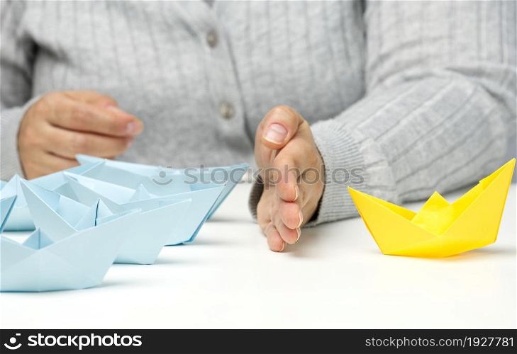 paper boats between a female hand on a white table. Conflict solution concept, negotiator between groups. Searching of decisions
