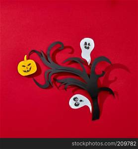 Paper branch, smiling scary pumpkin and ghosts on a red background with reflection of shadows and copy space. Creative handcraft Halloween card. Flat lay. Postcard for Halloween handcraft of paper ghosts and pumpkins with scary faces on a branch presented on a red background with reflection of shadows and space for text. Flat lay