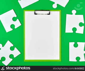 paper clip and white large paper puzzles on a green background, top view