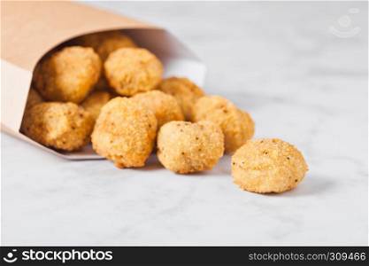 Paper container with fried crispy chicken popcorn nuggets on marble background
