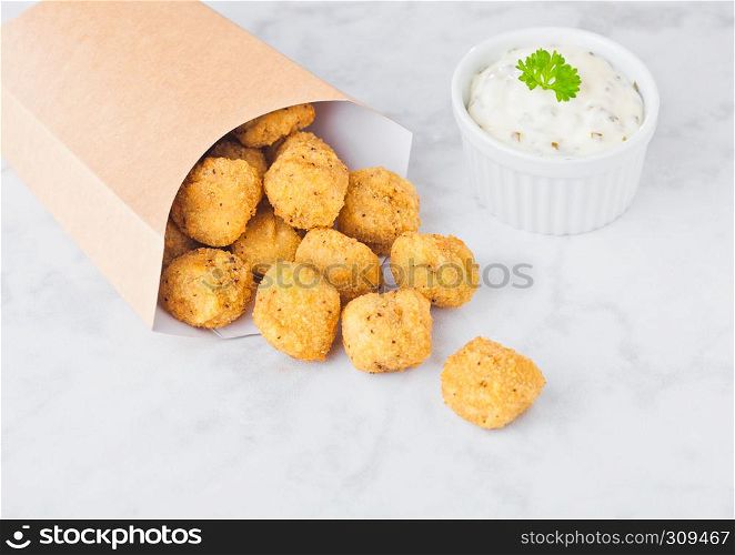 Paper container with fried crispy chicken popcorn nuggets on marble background with sauce