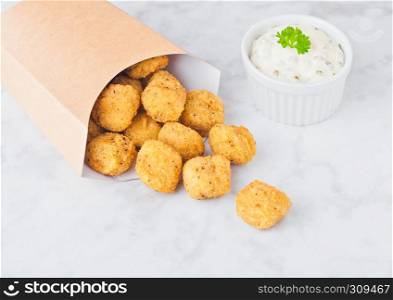 Paper container with fried crispy chicken popcorn nuggets on marble background with sauce