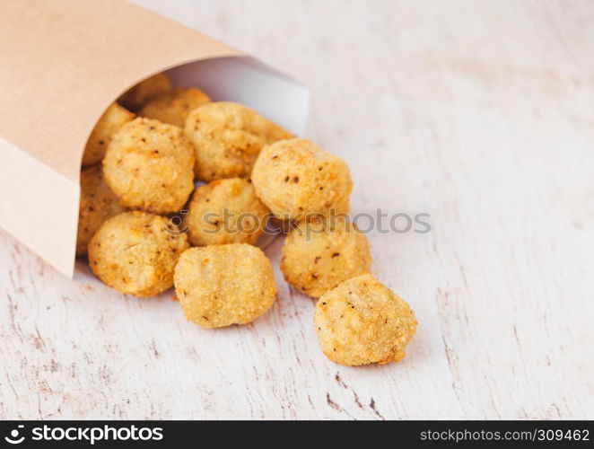 Paper container with fried crispy chicken popcorn nuggets on wooden background