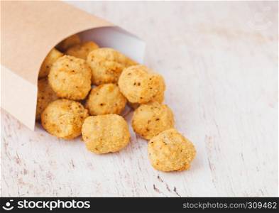 Paper container with fried crispy chicken popcorn nuggets on wooden background