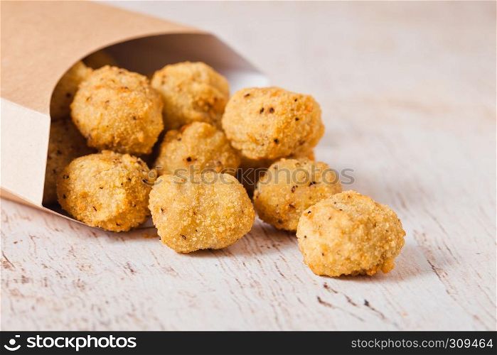 Paper container with fried crispy chicken popcorn nuggets on wooden background