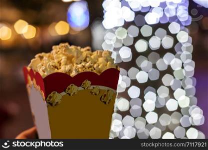 Paper cup with popcorn at night on lights background, close up