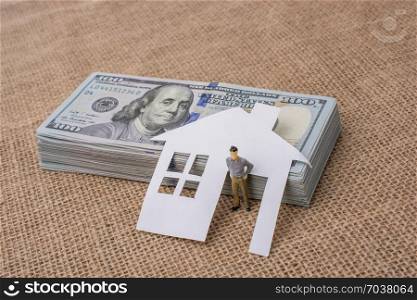 Paper house and a man figurine beside a bundle of US dollar banknote