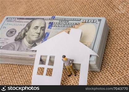 Paper house and a man figurine beside a bundle of US dollar banknote
