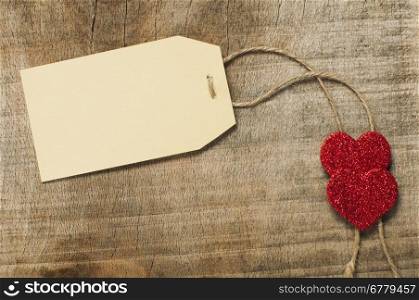 Paper label with rope and red hearts on wooden background