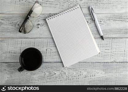 paper notebook,pen and Cup of tea or coffee and optical glasses on vintage shabby white wooden background. the view from the top. flat lay