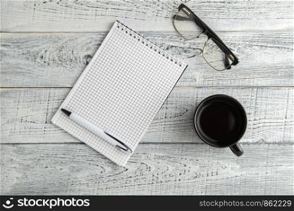 paper notebook,pen and Cup of tea or coffee and optical glasses on vintage shabby white wooden background. the view from the top. flat lay
