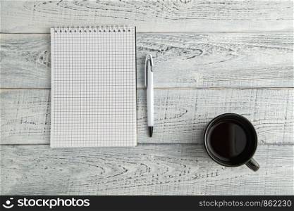 paper notebook,pen and Cup of tea or coffee on vintage shabby white wooden background. the view from the top. flat lay