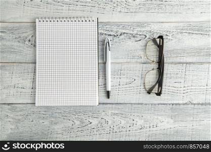 paper notebook,pen and optical glasses on vintage shabby white wooden background. the view from the top. flat lay