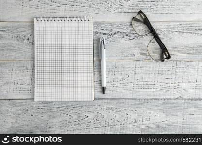 paper notebook,pen and optical glasses on vintage shabby white wooden background. the view from the top. flat lay