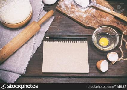 paper notepad with black pencil and dough with ingredients on a brown wooden table, vintage toning