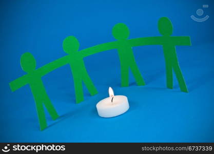 paper people holding hands and standing around burning candle