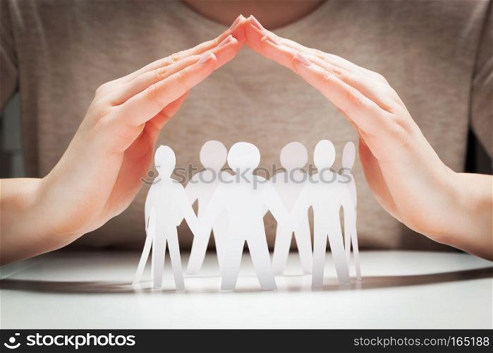 Paper people under hands in gesture of protection. Concept of insurance, social protection and support. . Paper people under hands in gesture of protection.. Concept of insurance