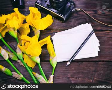 paper postcard and bouquet of yellow irises on a brown wooden background