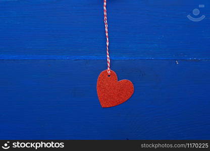 paper red shiny decorative hearts hanging on a rope on a dark blue wooden background, abstract holiday backdrop for valentines day on february 14. Decoration element