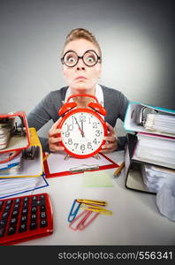 Paper work against time. Young expressive woman in office with big red clock. Unhappy businesswoman so far to ending her work.. Businesswoman in office with big red clock.