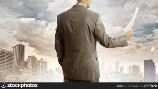 Paperwork. Back view of businessman reading documents in hand