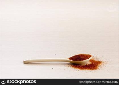 Paprika in a spoon with some spilt over the wooden background