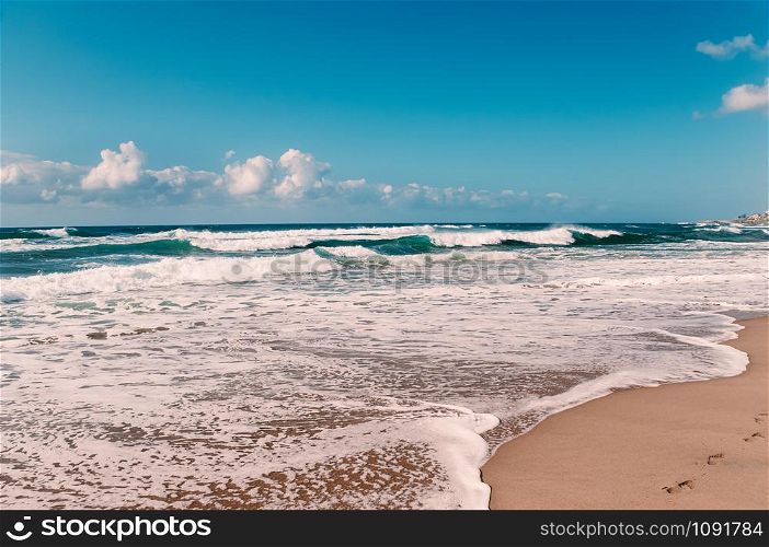 Paradise ocean beach, blue sky, white clouds, yellow sand, turquoise waves, panorama view, with footprints in wet sand