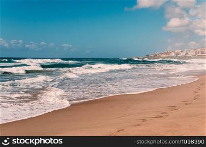 Paradise ocean beach, blue sky, white clouds, yellow sand, turquoise waves, panorama view, with footprints in wet sand, distant hotels in the background