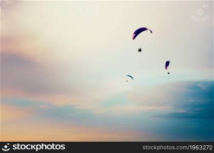Paragliders flying in the sky. Paragliding in the cloudy colorful sky at sunset. Extreme activity, hobby and sport