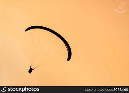Paragliding in the sunset sky. Silhouette of paraglider tandem flying in orange sky in the evening. Aerial view of paraglider in Oludeniz, Turkey. Extreme sport. Landscape. Concept. Silhouette of paraglider tandem flying in orange sky