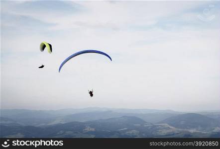 Paragliding. Two paragliders flying over mountains on cloudy sky background