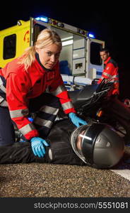 Paramedic assisting injured motorbike man driver on road at night