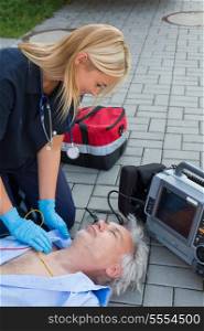 Paramedic examining unconscious elderly man lying on street