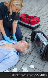 Paramedic examining unconscious elderly patient lying on street