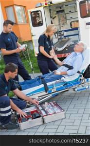 Paramedic team assisting injured senior man lying on stretcher outdoors