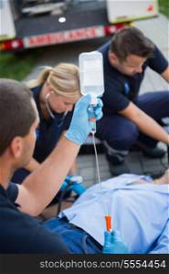 Paramedic team preparing drip for injured patient lying on street