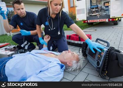 Paramedics checking pulse of unconscious senior man lying on street
