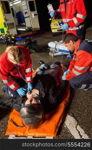 Paramedics examining injured motorcycle man driver on road at night