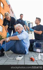 Paramedics giving firstaid to injured senior man sitting on street