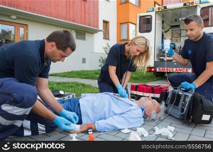 Paramedics giving firstaid to unconscious senior patient lying on ground