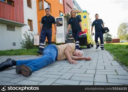 Paramedics giving help to injured senior man lying on street