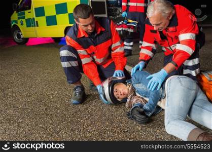 Paramedics helping injured motorbike woman driver lying on road night