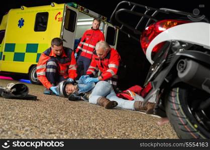 Paramedics helping injured motorcycle woman driver lying on road night