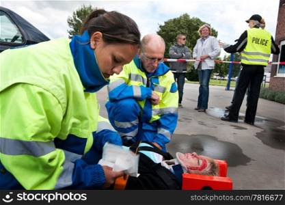 Paramedics providing first aid to an injured woman with police and bystanders in the background