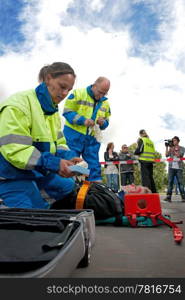 Paramedics tending to the first aid of an injured woman on a stretcher at the scene of a car crash, whilst a police woman talks to the bystanders behind the cordon tape, being filmed by a camera man