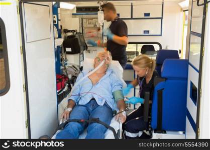 Paramedics treating unconscious elderly man on stretcher in ambulance car