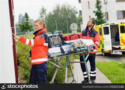 Paramedics with medical equipment ringing doorbell ambulance house call aid