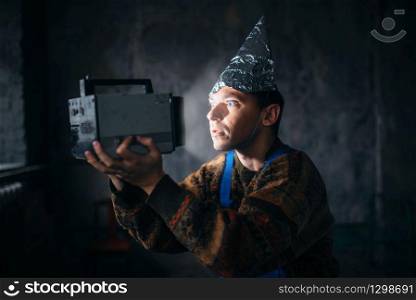 Paranoid man in tinfoil cap watch TV, mind protection from telepathy, paranoia concept. UFO phobia, conspiracy theory