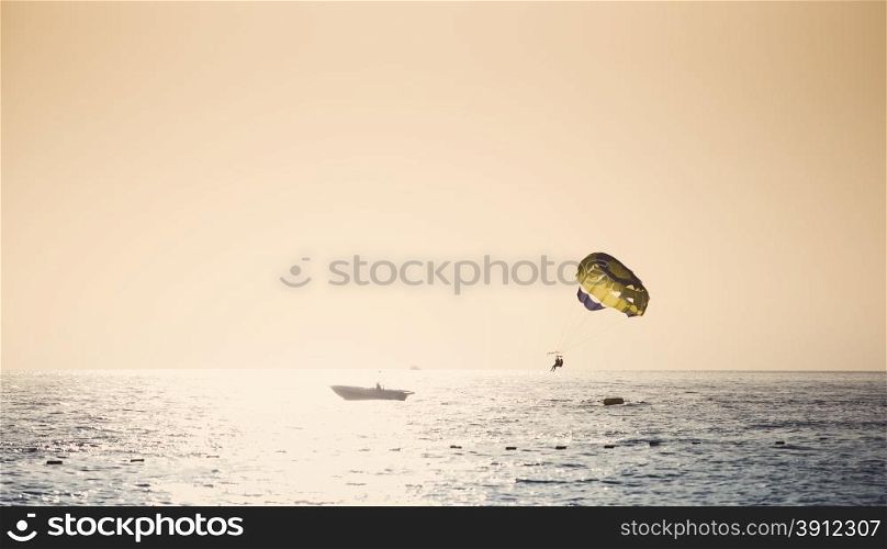 Parasailing on parachute over water at sunset